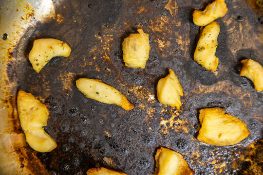 Burnt cooking oil with chicken breast pieces in stainless steel frying pan