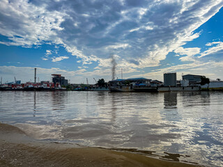 Fototapeta premium Blue sky with fluffy clouds above flooded village. Brown water surrounds wooden houses and tall power lines. No people visible, so emotions unobservable.