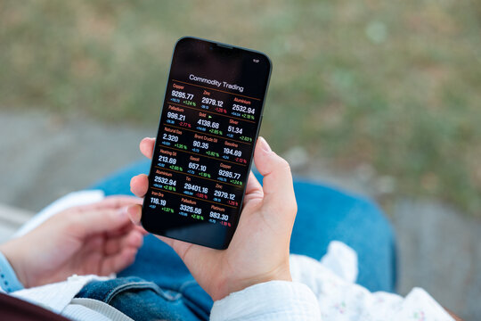 Woman is sitting on a park bench, checking commodity prices on her smartphone, digital commodity trading. Stock market and exchange, internet, mobile app, wireless technology.