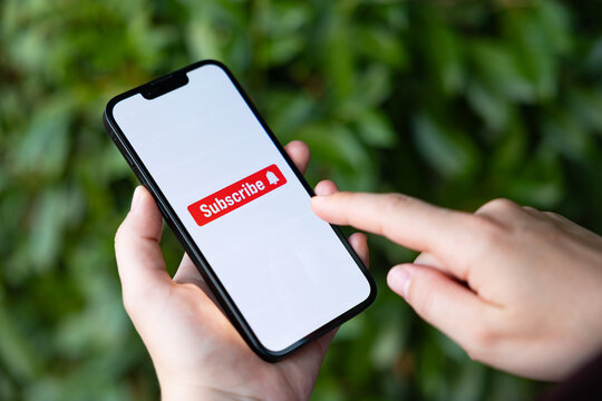 Subscribe icon, a woman in the park with a smartphone taps the subscribe button on the screen, social media. Internet, newsletter, e-commerce, mobile app, wireless technology.