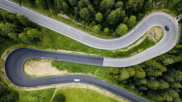 Aerial view of a winding mountain road with sharp hairpin turns through dense pine forests in Canazei, Trentino-Alto Adige, Italy.