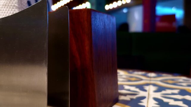 Warm string lights add a soft glow around the dark wooden divider and metallic panel. The colorful blurred interior forms an atmospheric setting with layered textures and subtle visual contrast.