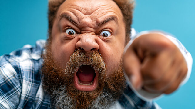 Angry bearded man wearing plaid shirt shouting aggressively and pointing finger forward
