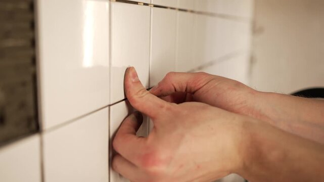 Close-up view of a skilled construction worker's hands meticulously installing white ceramic tiles, using plastic crosses as spacers to ensure precise and uniform grout lines