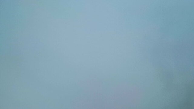 The aerial view from an airplane shows agricultural fields partly obscured by thick, misty white clouds. Faint roads and greenery remain visible through the cloud cover, adding depth to the scene.