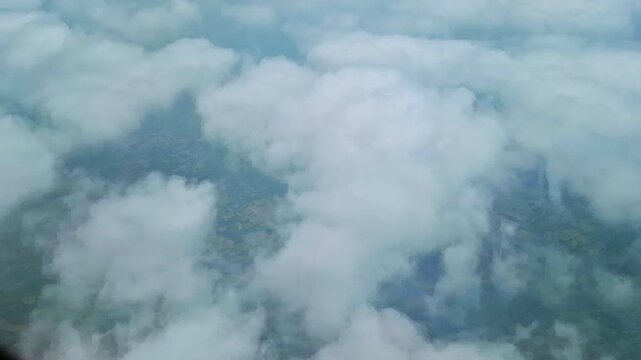 The aerial view from an airplane shows dense white clouds over green agricultural fields. Faint portions of the landscape appear through cloud gaps, creating a soft and atmospheric rural scene.