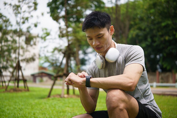Fototapeta premium Young Asian athlete checking a smartwatch while resting after exercise.