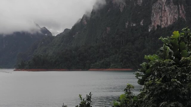 Ratchaprapha Dam on a rainy day at khao sok national park, surat thani province thailand featuring spectacular limestone mountains shrouded in mist.