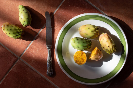 Fresh prickly pears are lying on an old plate in the kitchen. Some of the prickly pears have been cut open. The photo was taken from above.