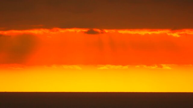Bright burning light radiates across the distant sea horizon as soft dark storm clouds drift above. Static medium shot.