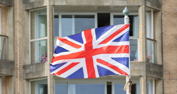 Union Jack Flag Waving On A Pole In Front Of Residential Building Exterior In The UK
