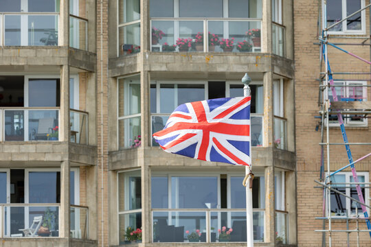 Union Jack Flag Waving On A Pole In Front Of Residential Building Exterior In The UK