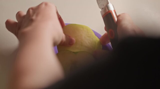 Close up of hands slicing green apples into thin rounds. Process involves using both manual knife work. Plain background keeps focus entirely on hand movements with apple