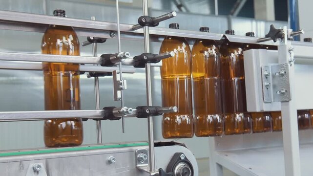 Industrial bottling line with brown glass bottles moving along conveyor through clean beverage plant beside filling and capping machinery in bright orderly workspace