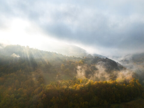 Aerial view of mountain forests shrouded in morning mist with dramatic sunbeams breaking through the clouds