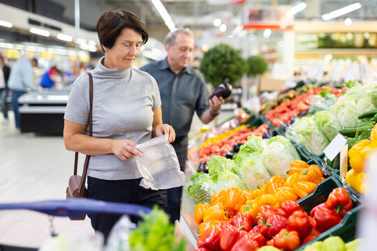 elderly woman chooses pepper in vegetable and fruit department
