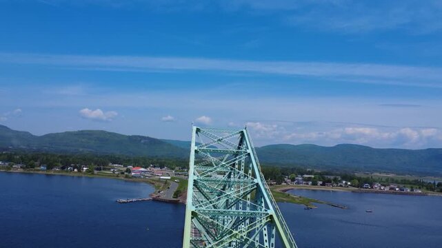 Drone ascent rising along the steel structure of the J.C. Van Horne Bridge, revealing a sweeping view toward the Gasp&eacute; mountains near the Listuguj Mi'gmaq First Nation reserve in Gasp&eacute;sie, Quebec.