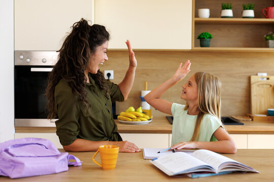 Mother and daughter in a bright kitchen sharing a happy high five, celebrating a learning achievement and feeling positive connection during schoolwork