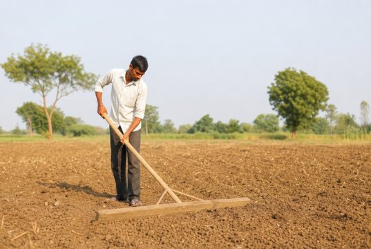 Hardworking young farmer manually plowing fertile brown soil with traditional wooden plow in rural field under bright sunny sky, agricultural labor concept