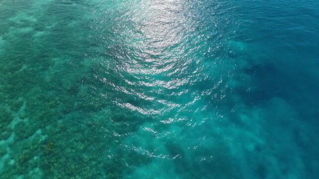 Beautiful tropical sea surface texture with sparkling sunlight and underwater coral, cinematic drone shot.