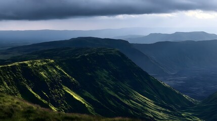 Fototapeta premium A dramatic mountain landscape under heavy clouds with deep green slopes and layered valleys stretching into the distance