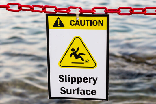 Caution Slippery Surface Sign Hanging on Red Chain Over Water Near Dock or Shore