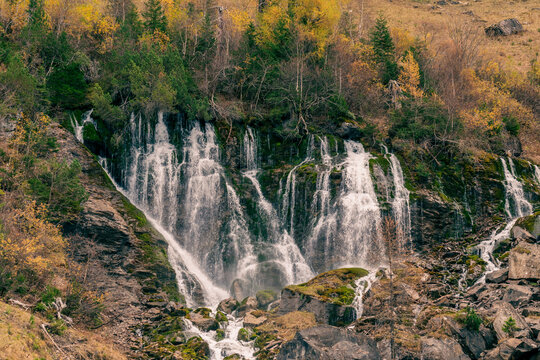 Cascading mountain water over rocky cliffs surrounded by colorful fall foliage in Switzerland.