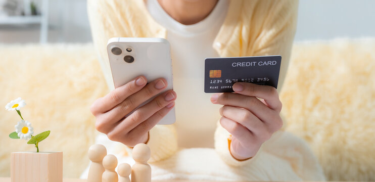 Person using smartphone and credit card for online payment at home with family figures, representing digital banking, cashless finance, secure transactions, shopping and financial services.