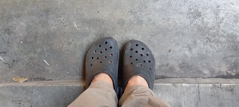 Top-Down Point of View of a Person Wearing Black Rubber Clogs Standing on a Weathered Concrete Floor