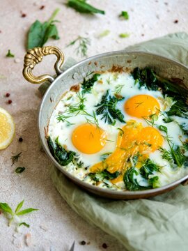 Fried eggs with spinach in a rustic metal pan for a healthy breakfast or brunch meal.