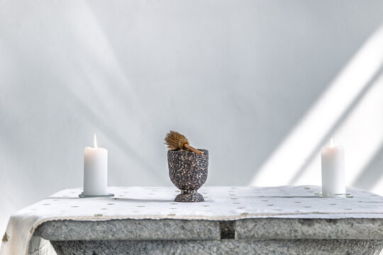 Lit Candles and Holy Water Aspergillum in Chalice on Stone Altar with Soft Sunlight