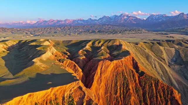 Aerial view of layered rock formations and colorful Danxia landforms under a golden sunset along the S101 highway in Xinjiang, China.