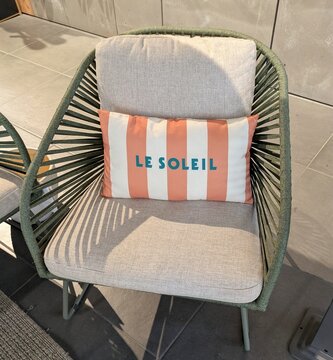 Rinc&oacute;n de una terraza con un sill&oacute;n de exterior con estructura y laterales de cuerdas tensadas, con respaldo y asiento acolchados y un coj&iacute;n, con una alfombra trenzada