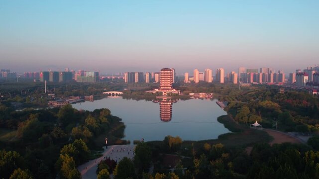 A serene urban landscape featuring a pagoda by a calm lake, surrounded by green trees and distant city buildings at dawn.