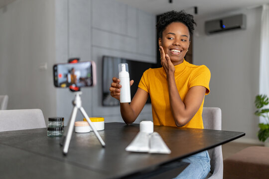 Woman sitting at a table giving skincare tips while recording a video at home