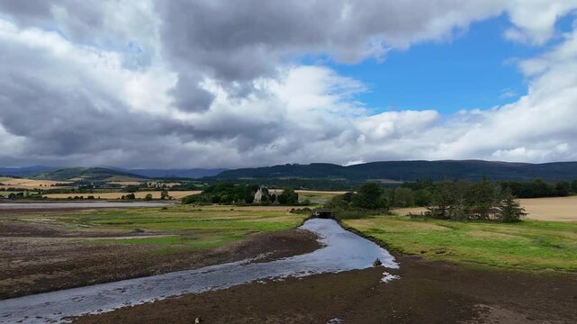 Wide angle aerial drone video of river stream flowing towards Cromarty Firth with Kiltearn Old Parish Church in background, Evanton, Scottish Highlands, Scotland, UK