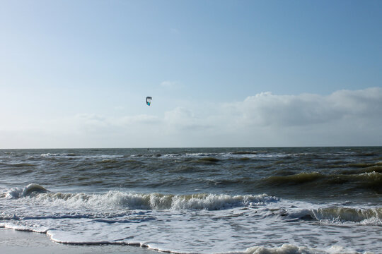 Kitesurfer conquers the waves at the North Sea beach on a sunny day with a fresh breeze, capturing a crisp and energetic scene