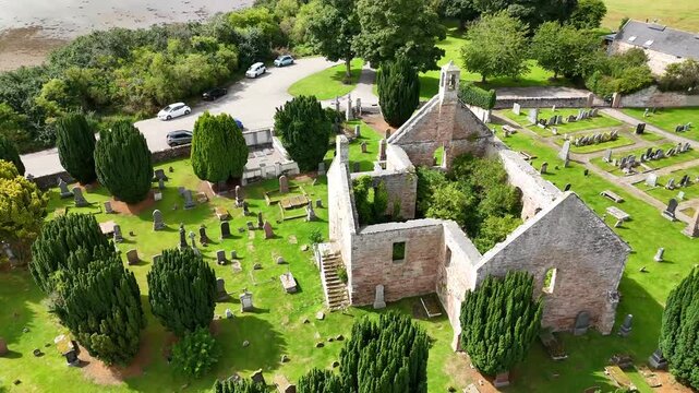 Elevated close aerial drone video of Kiltearn Old Parish Church roofless stone ruins, bellcote, external stairs, and surrounding graveyard, Evanton, Scottish Highlands, Scotland, UK