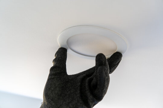 Electrician installing a recessed ceiling light fixture in a white ceiling during interior renovation.