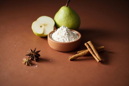 Pear, cinnamon and flour arranged at a 45 degree angle on a terracotta surface