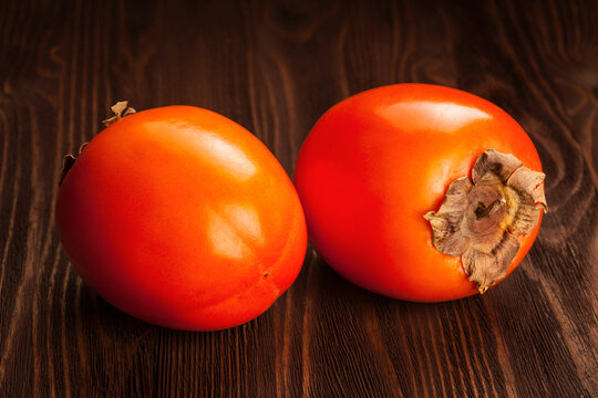 Scene featuring two fresh ripe orange persimmon on a wooden background