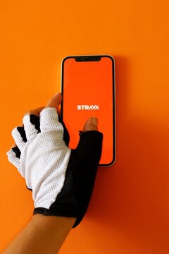 Salvador, Brazil - August 16, 2026: Hand of an athlete wearing a cycling glove and holding a smartphone displaying the Strava app, a popular fitness tracking application. Strava logo.