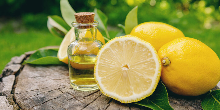Lemon essential oil bottle with dropper and fresh yellow lemons on a wooden stump