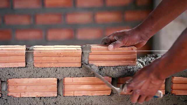 Construction worker laying bricks and applying mortar with trowel, building brick wall, steady progress, detailed shot, masonry work in progress.
