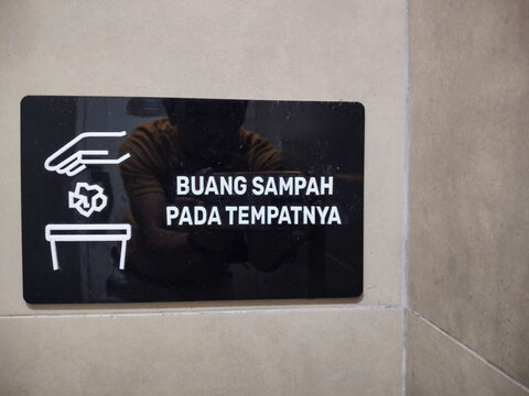 An information sign affixed to a wall, urging people to dispose of trash in the proper receptacles.