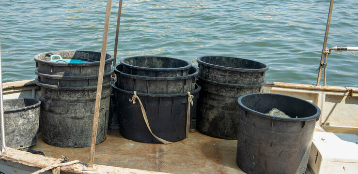 Fishing gear and heavy duty black plastic tubs stacked on the deck of a commercial fishing vessel on the water