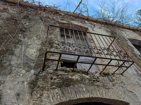 Ornate iron balcony above arched brick entrance of ruined historical property surrounded by vines