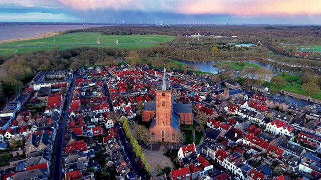 High angle aerial drone video clip of historic Naarden town center, Great Church Grote Kerk, red roof houses, moat water canal, sunset sky, and car parking lot in Netherlands, West Europe