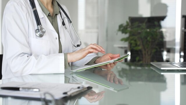 Doctor woman accessing patient data on digital tablet, managing healthcare records in modern medical office. Medicine, health care and science concept