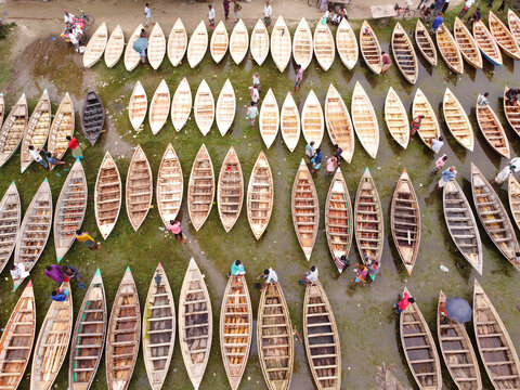 Manikganj, Dhaka Division, Bangladesh - 25 August 2021: Aerial view of Bost Market featuring numerous wooden boats lined up on the muddy ground with people walking between them.